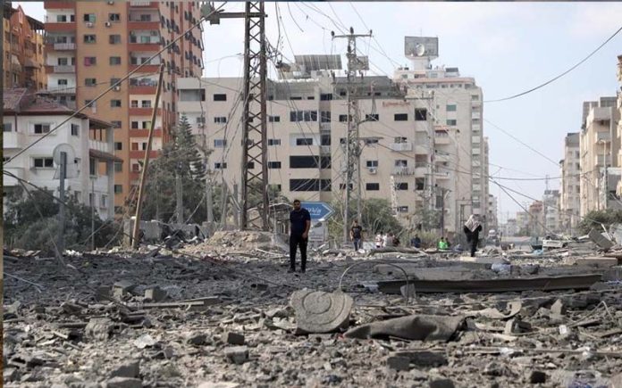 10月10日，在加薩走廊人們走過被以色列空襲炸毀的建築廢墟。（圖自新華社）